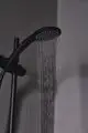 Schwarze Handbrause von Ideal Standard mit gleichmäßigem Wasserstrahl, montiert an einem senkrechten Halter. Dekorative Wandfläche im Hintergrund.